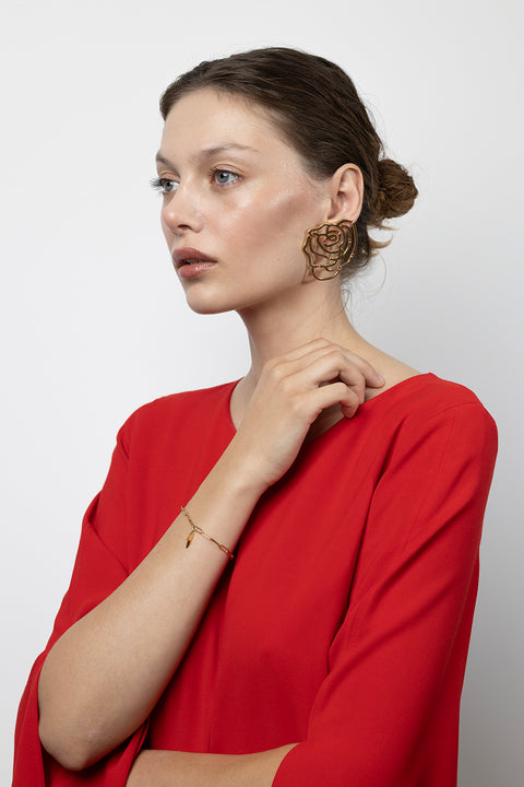 Ta minimalistyczna bransoletka na łańcuszku z kolekcji PROFONDO ROSSO UMIAR biżuteria wyróżnia się elegancką zawieszką inspirowaną cierniem róży. Subtelnie inkrustowany naturalnym rubinem o średnicy 2 mm i masie 0,05 ct dodaje jej wyjątkowego charakteru. Wykonana ręcznie ze szlachetnych materiałów: srebra 925 i srebra 925 pozłacanego 24-karatowym złotem. Inspiracją dla kolekcji była uroda róży, tworząc unikalne formy biżuteryjne i modne apaszki, które rozkładają ją na czynniki pierwsze.