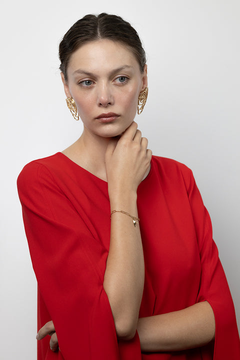 Ta minimalistyczna bransoletka na łańcuszku z kolekcji PROFONDO ROSSO UMIAR biżuteria wyróżnia się elegancką zawieszką inspirowaną cierniem róży. Subtelnie inkrustowany naturalnym rubinem o średnicy 2 mm i masie 0,05 ct dodaje jej wyjątkowego charakteru. Wykonana ręcznie ze szlachetnych materiałów: srebra 925 i srebra 925 pozłacanego 24-karatowym złotem. Inspiracją dla kolekcji była uroda róży, tworząc unikalne formy biżuteryjne i modne apaszki, które rozkładają ją na czynniki pierwsze.