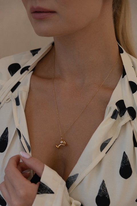 Odkryj nasz wyjątkowy naszyjnik od UMIAR biżuteria, zainspirowany kształtem kieliszka do martini, stworzony z myślą o otwarciu Jewellery Bar - ekskluzywnego butiku marki, łączącego wyjątkowy design z atmosferą barową. Jego głównym elementem jest naturalna perła, nawiązująca do charakterystycznej oliwki w tym popularnym drinku. Długość łańcuszka wynosi 50 cm. Całkowicie wykonany ręcznie ze szlachetnych materiałów: srebra 925 oraz srebra 925 pozłacanego 24-karatowym złotem.