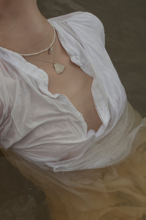 Wyjątkowy naszyjnik choker, stworzony z połączenia srebrnego łańcuszka, delikatnego wisiorka w kształcie połamanej muszli i naturalnych pereł. Regulowana długość łańcuszka pozwala nosić go przy szyi lub nieco niżej. Ręcznie wykonany ze szlachetnych materiałów przez UMIAR biżuteria. Dostępny w dwóch wariantach: srebrze 925 i srebrze 925 pozłacanym 24-karatowym złotem.